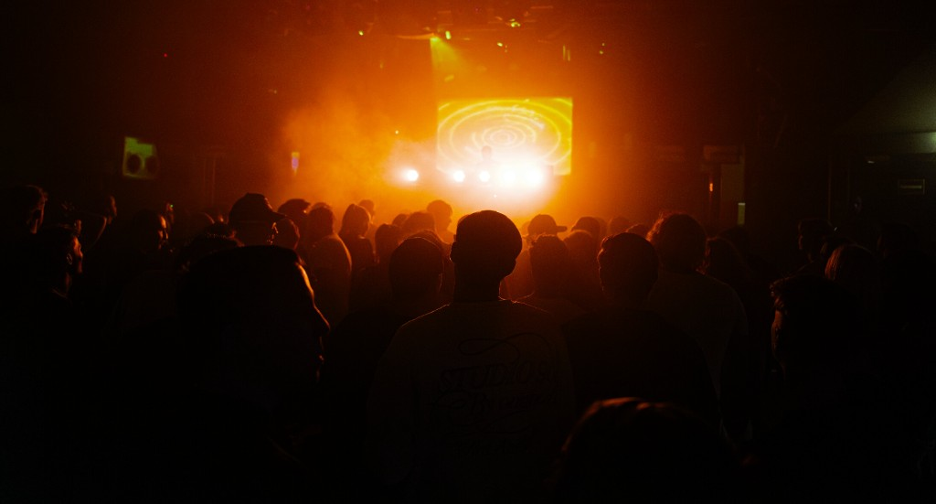 Publikum vor der Bühne bei einem Clubevent in orangem Bühnenlicht